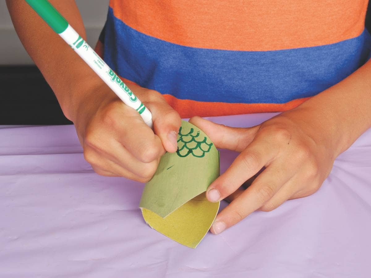 hands draw the snake's scales on the toilet roll tube with a felt pen