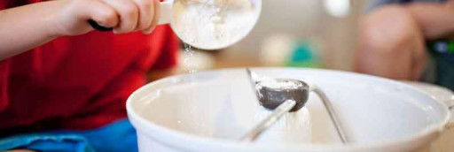 A child adding a scoop of flour to a food mixer.