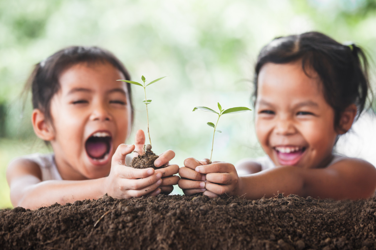 Two children smiling at a plant growing