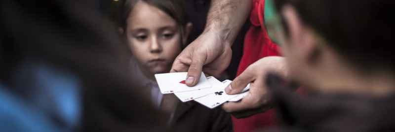 A young girl among a crowd watching as a man performs a card trick.