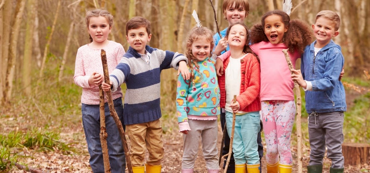 A group of children holding sticks as they pose for a picture in the woods.
