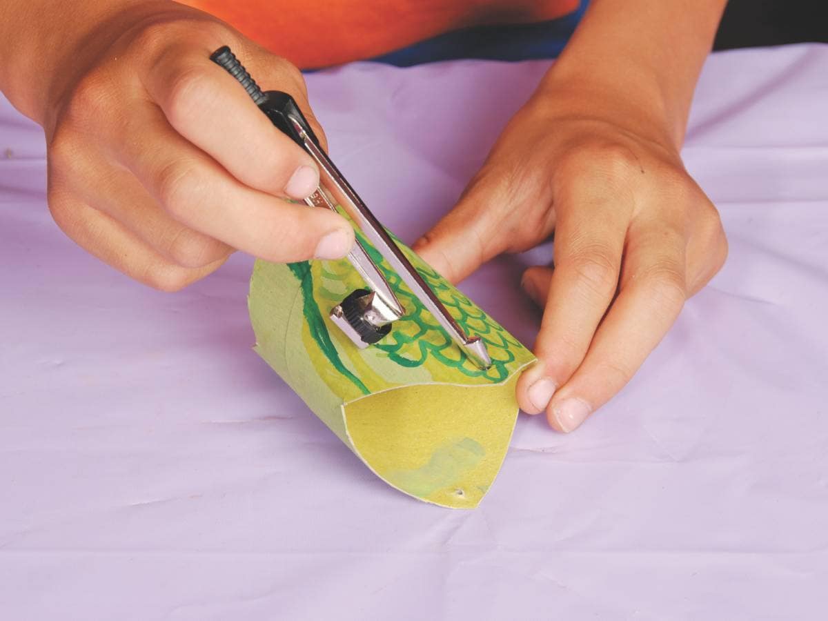 hands use a compass to poke holes in the toilet rolls 