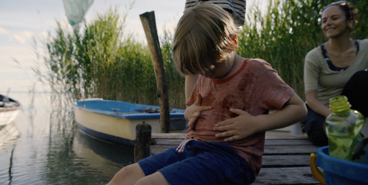 Little boy sat by a lake getting his t-shirt dirty