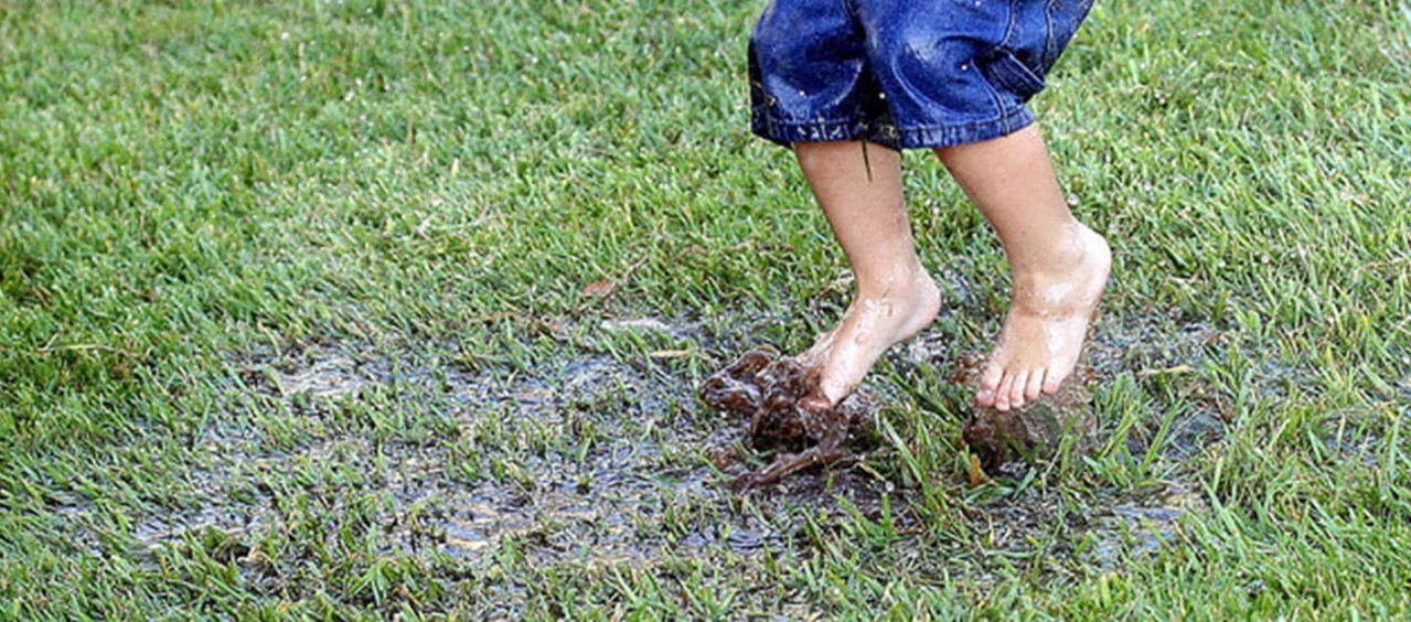 A child jumping barefoot in a muddy puddle.