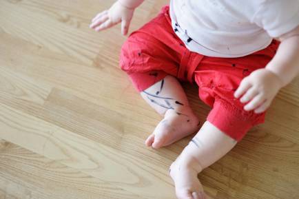 A baby's legs and clothes covered in pen stains.