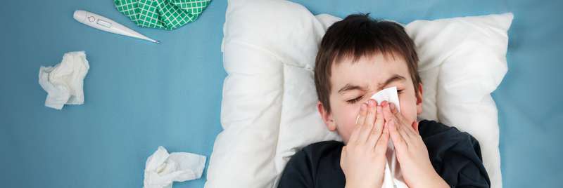Child in bed sneezing into a tissue