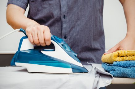 A man ironing a shirt with colourful towels beside him.