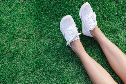 A pair of legs wearing clean white plimsolls, sitting on the grass.
