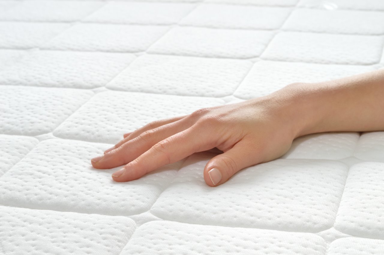 A hand resting on a clean white mattress.