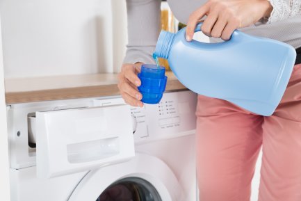 Woman in pink trousers pouring fabric conditioner into a bottle cap.