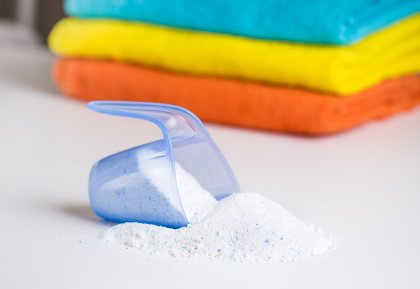 A scoop of washing powder in front of a pile of folded towels.