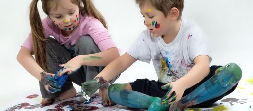 A girl and boy getting messy painting with their hands and feet.