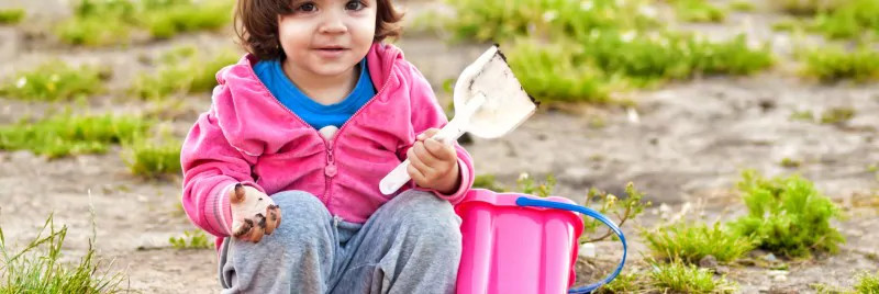 A young girl with muddy hands playing with a bucket and spade.