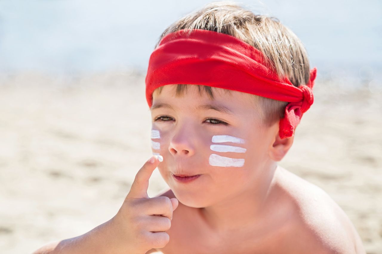 A boy in a red bandana drawing white warrior stripes on his face.